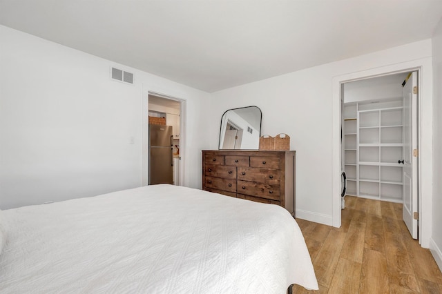 bedroom with a spacious closet, visible vents, light wood-type flooring, freestanding refrigerator, and a closet