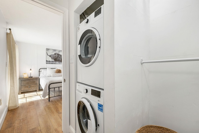 clothes washing area featuring laundry area, light wood-style floors, and stacked washer and clothes dryer