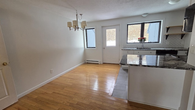 kitchen with tasteful backsplash, baseboards, baseboard heating, light wood-style floors, and a textured ceiling