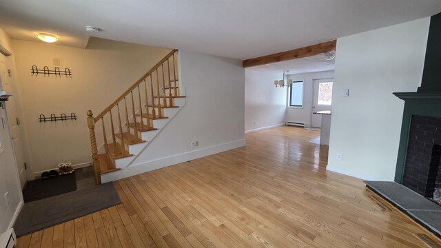 unfurnished living room with a baseboard heating unit, light wood finished floors, baseboards, a brick fireplace, and stairs