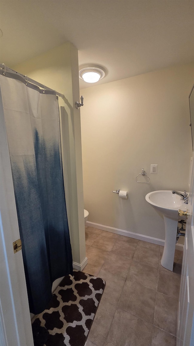 bathroom featuring a shower with shower curtain, toilet, baseboards, and tile patterned floors