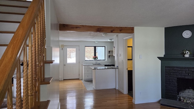 kitchen with decorative backsplash, a brick fireplace, light wood-type flooring, and a textured ceiling