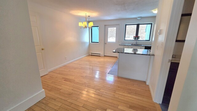 kitchen with baseboards, a chandelier, dark stone countertops, light wood-style flooring, and a baseboard radiator