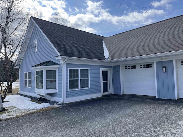 cape cod house featuring board and batten siding, driveway, a garage, and roof with shingles