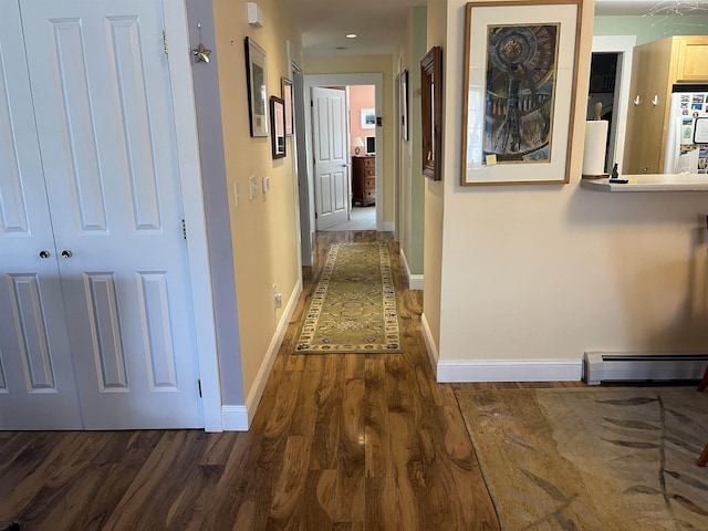 corridor with a baseboard heating unit, baseboards, and dark wood-type flooring