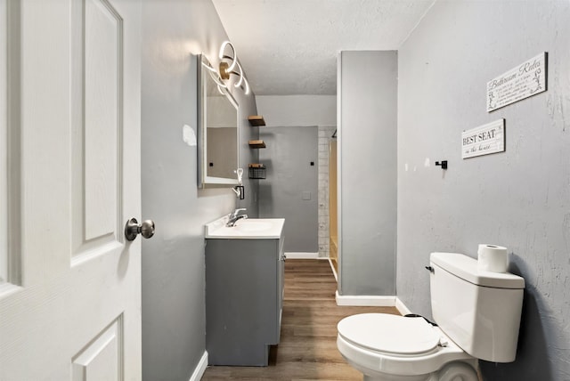 bathroom with toilet, wood finished floors, a shower, baseboards, and vanity