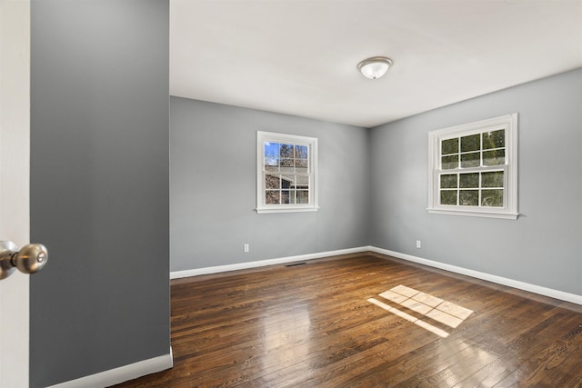 unfurnished room with a wealth of natural light, visible vents, baseboards, and wood finished floors