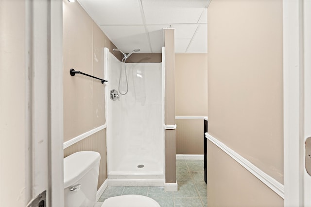 bathroom featuring a wainscoted wall, a drop ceiling, tile patterned flooring, a walk in shower, and toilet