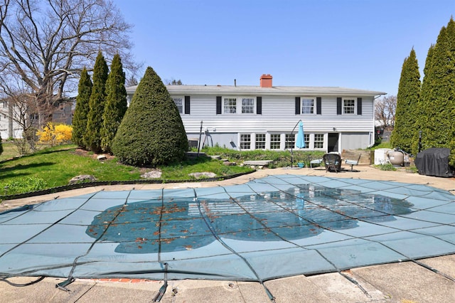 rear view of property featuring a covered pool, a patio, and a chimney