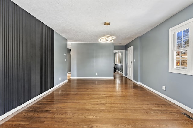 unfurnished room featuring visible vents, an inviting chandelier, baseboards, and wood finished floors