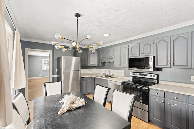 kitchen featuring light wood-style flooring, gray cabinets, a sink, stainless steel appliances, and crown molding