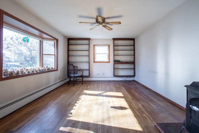 empty room featuring a baseboard radiator, baseboards, hardwood / wood-style floors, and a wood stove