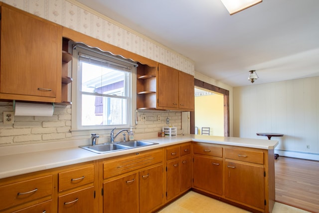 kitchen featuring open shelves, light countertops, a peninsula, brown cabinetry, and a sink