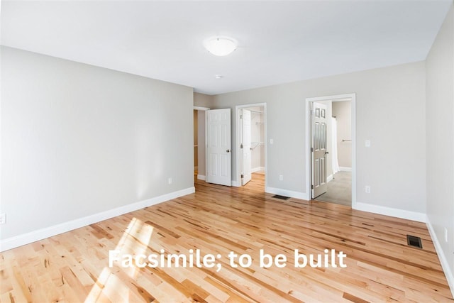 unfurnished bedroom featuring a spacious closet, wood finished floors, visible vents, and baseboards