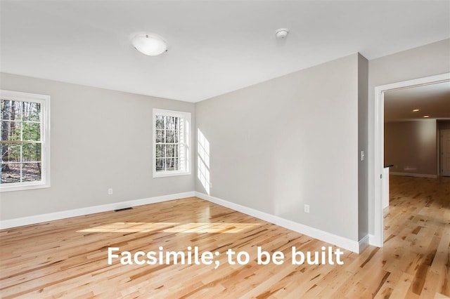 spare room with wood finished floors, a healthy amount of sunlight, visible vents, and baseboards