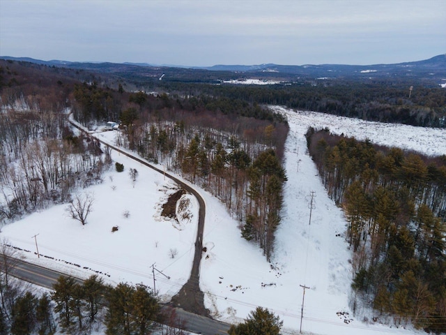 snowy aerial view with a wooded view and a mountain view