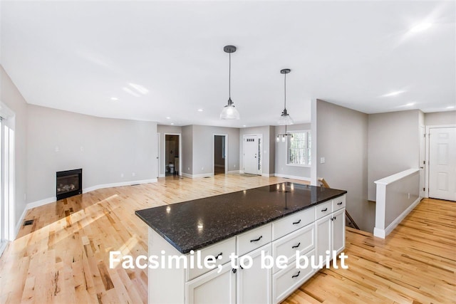 kitchen featuring a glass covered fireplace, dark stone counters, light wood-style flooring, hanging light fixtures, and white cabinetry