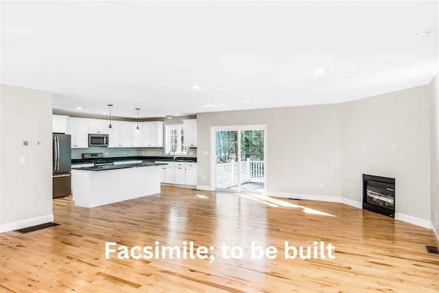 kitchen with dark countertops, a center island, white cabinetry, light wood-style floors, and appliances with stainless steel finishes