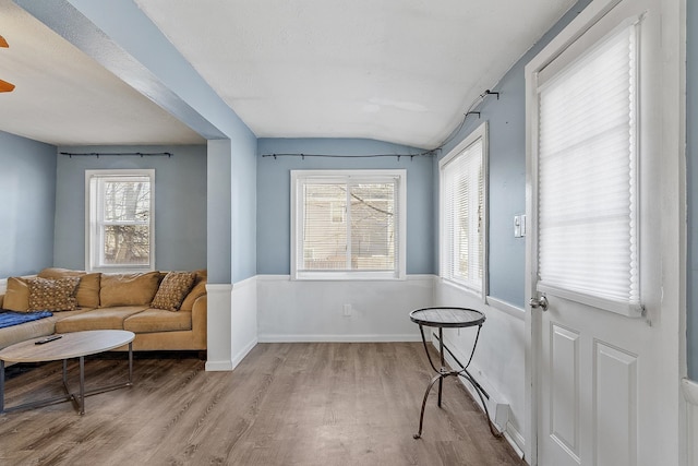 living area featuring light wood-style flooring, baseboards, and vaulted ceiling