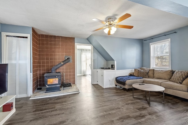 living area with a ceiling fan, wood finished floors, a wood stove, a textured ceiling, and tile walls