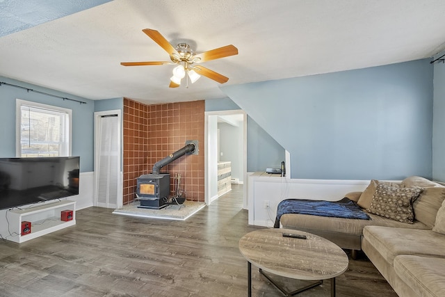 living room with ceiling fan, a textured ceiling, wood finished floors, and a wood stove