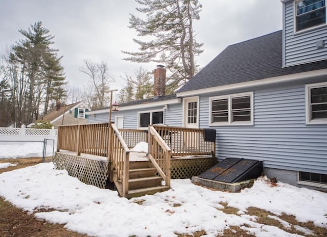 snow covered rear of property featuring a shingled roof, fence, a chimney, and a wooden deck