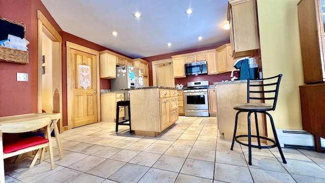 kitchen featuring light tile patterned floors, light brown cabinetry, appliances with stainless steel finishes, a kitchen bar, and a center island