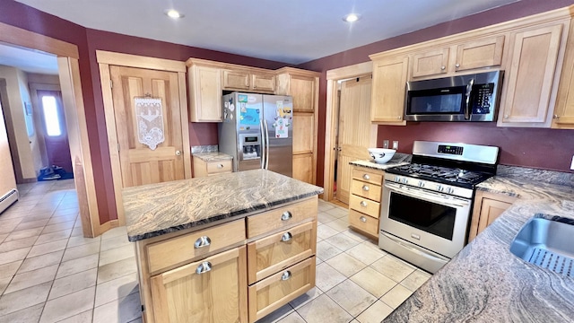 kitchen with light brown cabinets, light stone counters, a kitchen island, appliances with stainless steel finishes, and light tile patterned floors