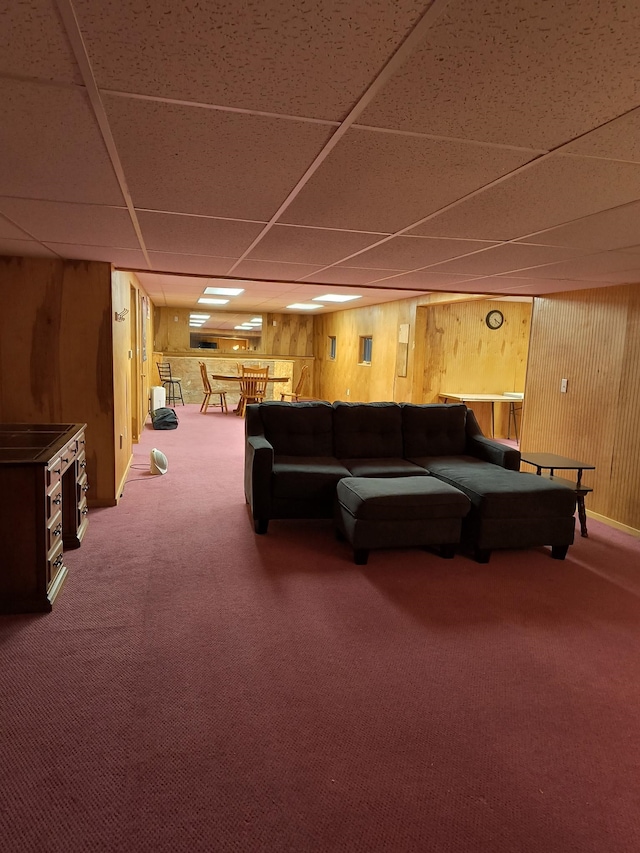 carpeted living room with wooden walls and a paneled ceiling