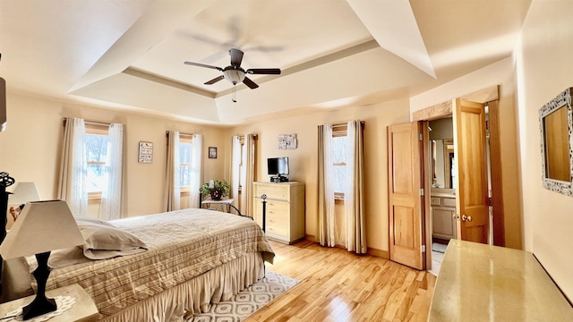 bedroom with baseboards, light wood-type flooring, a tray ceiling, and a ceiling fan