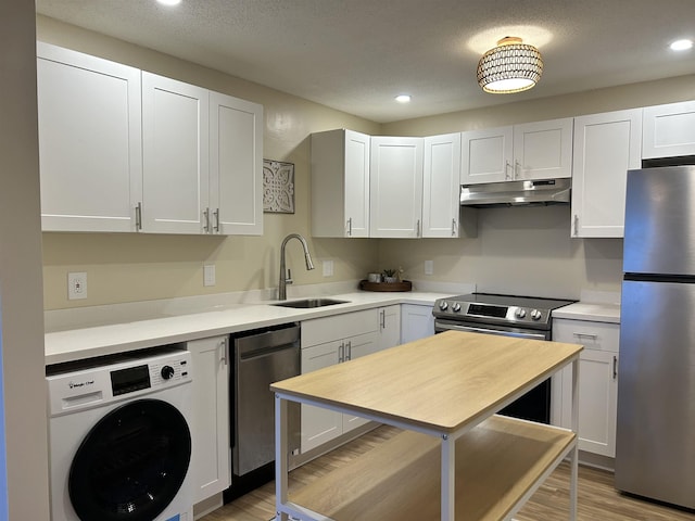 kitchen with under cabinet range hood, light countertops, washer / dryer, stainless steel appliances, and a sink