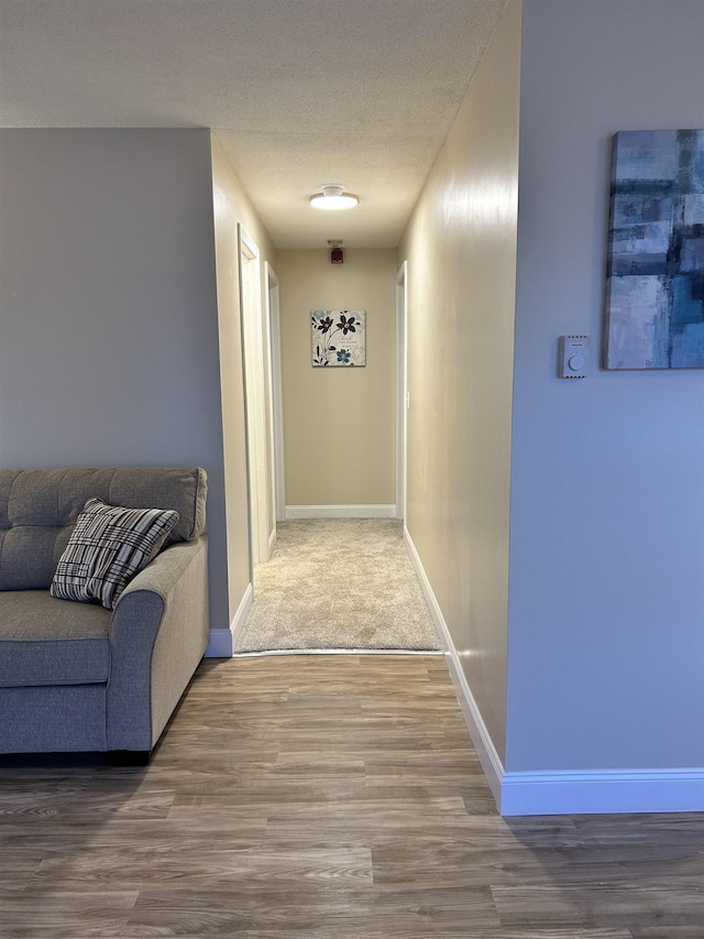 hall featuring a textured ceiling, baseboards, and wood finished floors