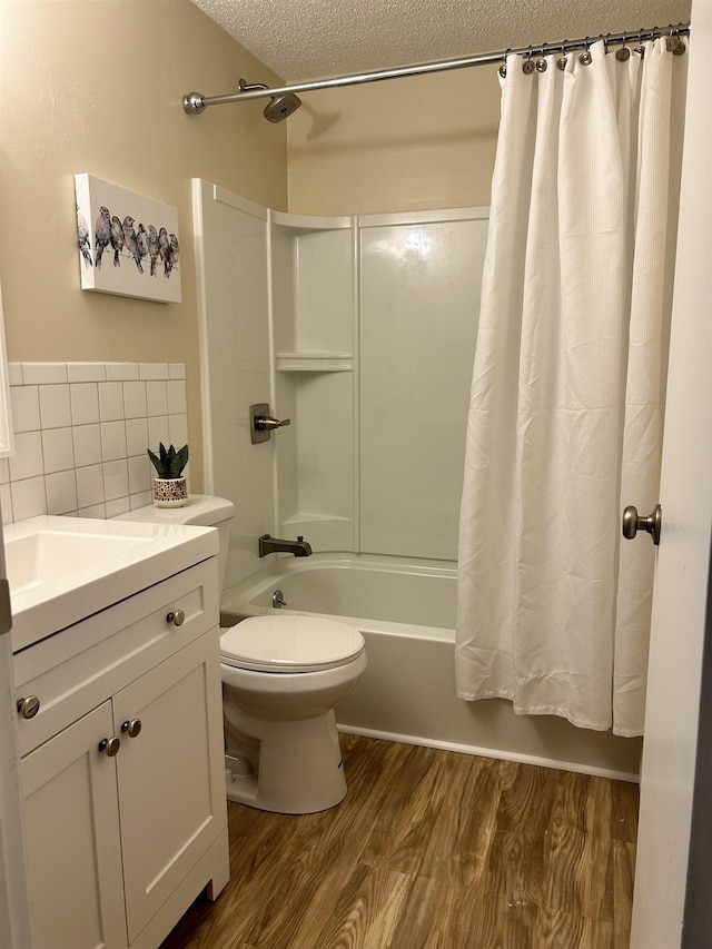 full bath with toilet, a textured ceiling, wood finished floors, shower / bath combination with curtain, and vanity