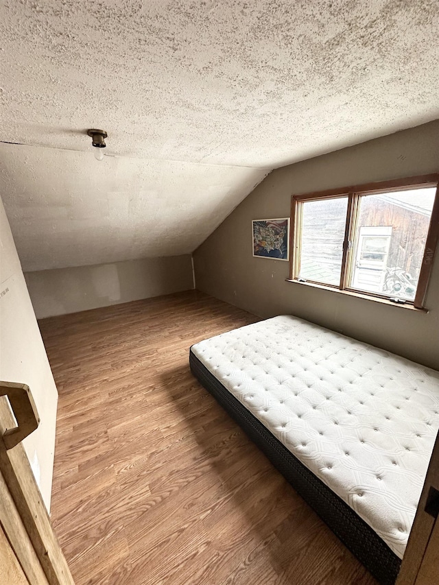 unfurnished bedroom featuring lofted ceiling, a textured ceiling, and wood finished floors