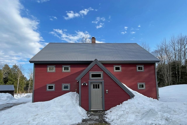 snow covered rear of property with metal roof and a chimney