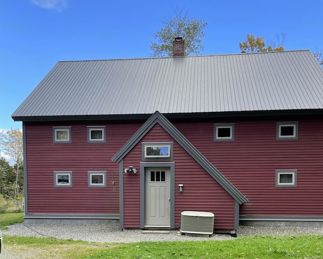 back of house with a chimney, central AC, and metal roof