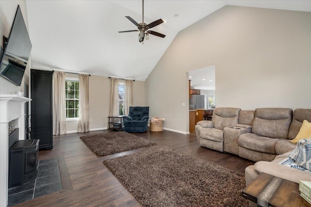 living area with high vaulted ceiling, dark wood-style floors, baseboards, ceiling fan, and a wood stove