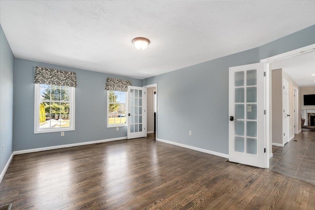 spare room with dark wood finished floors, a fireplace, french doors, and baseboards