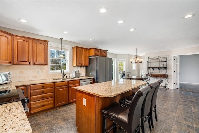 kitchen with brown cabinetry, a kitchen island, a sink, decorative backsplash, and appliances with stainless steel finishes