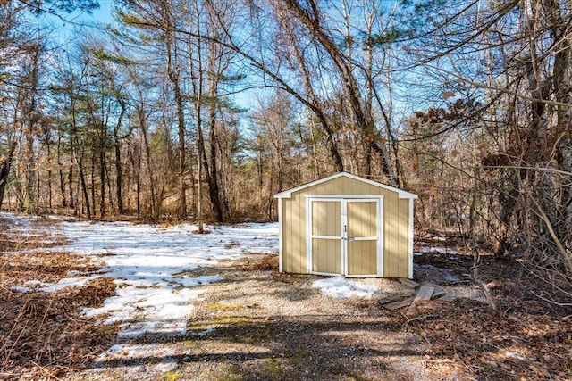 snow covered structure with a storage unit, an outbuilding, and a wooded view