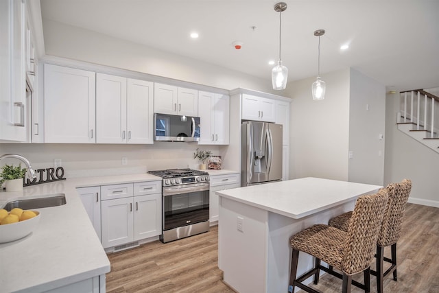 kitchen with a breakfast bar area, light wood finished floors, a sink, stainless steel appliances, and white cabinetry