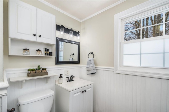 half bathroom with a wealth of natural light, toilet, wainscoting, and crown molding