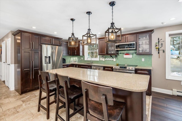 kitchen featuring dark brown cabinetry, a wealth of natural light, decorative backsplash, stainless steel appliances, and a sink