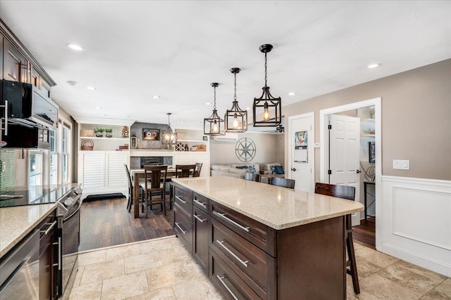 kitchen with dark brown cabinetry, decorative light fixtures, dishwasher, a breakfast bar area, and wainscoting