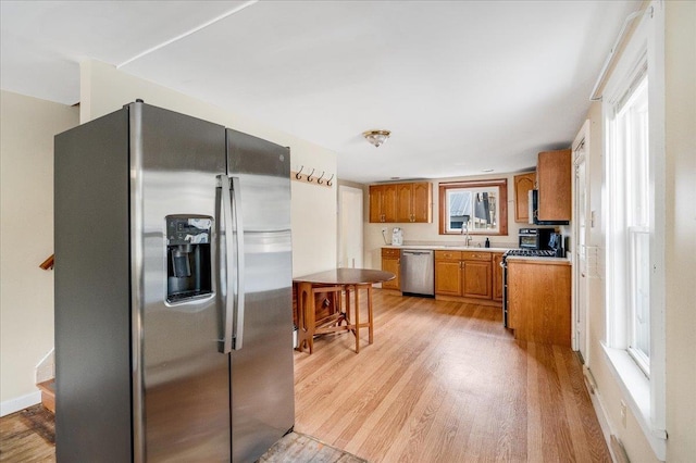 kitchen with brown cabinetry, a sink, stainless steel appliances, light countertops, and light wood-style floors