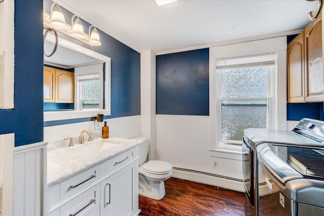 bathroom featuring toilet, a baseboard heating unit, washing machine and dryer, wood finished floors, and wainscoting