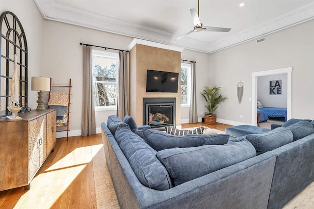 living room featuring visible vents, ceiling fan, crown molding, light wood-type flooring, and a large fireplace