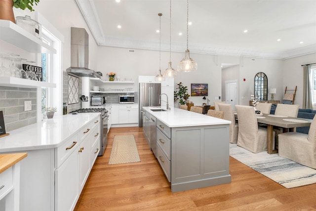 kitchen with open shelves, gray cabinets, stainless steel appliances, wall chimney exhaust hood, and a sink