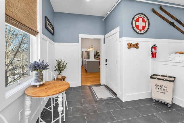 entrance foyer featuring dark tile patterned flooring, wainscoting, and a decorative wall