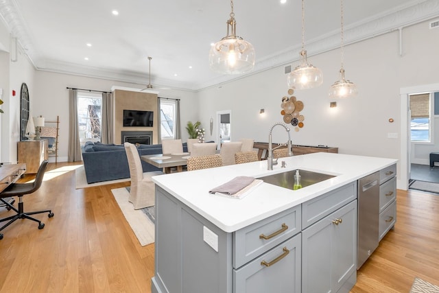 kitchen with light wood-style flooring, an island with sink, a fireplace, gray cabinets, and a sink